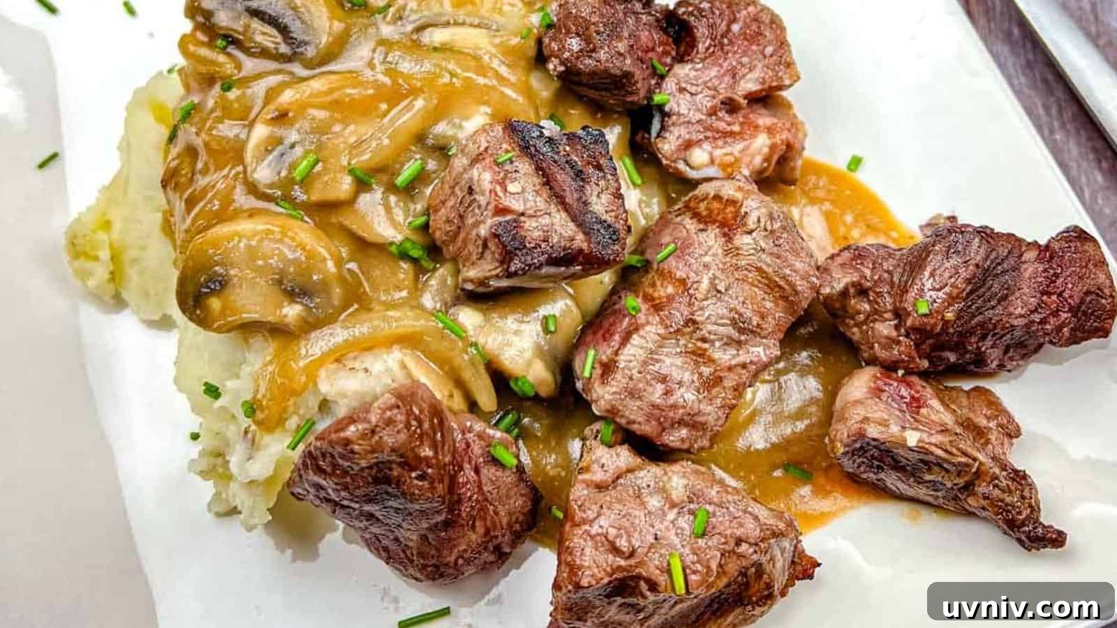 Texas Roadhouse Beef Tips with mushroom gravy over mashed potatoes, garnished with chives on a white plate.