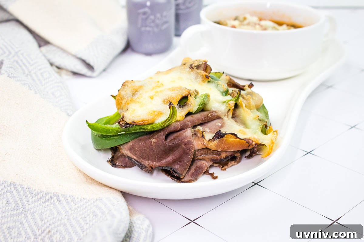 A white plate with a Philly Cheesesteak Stack and a bowl of soup.