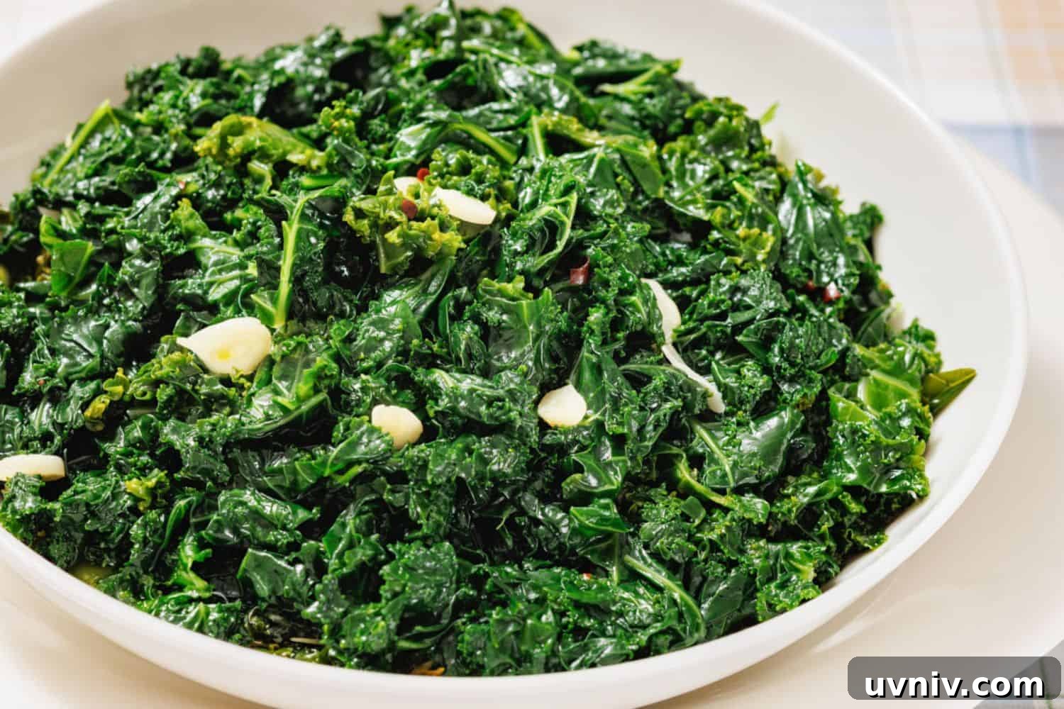 A white bowl filled with sautéed kale and sliced garlic on a light-colored surface.
