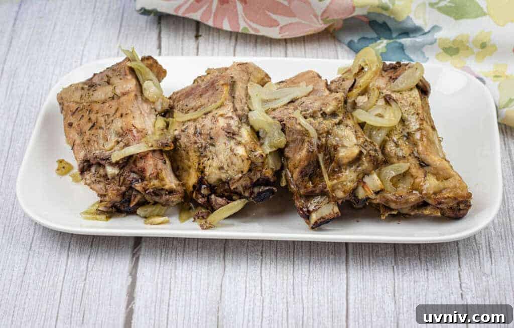 Oven-baked ribs with onion and garlic on top served on a white rectangular plate.