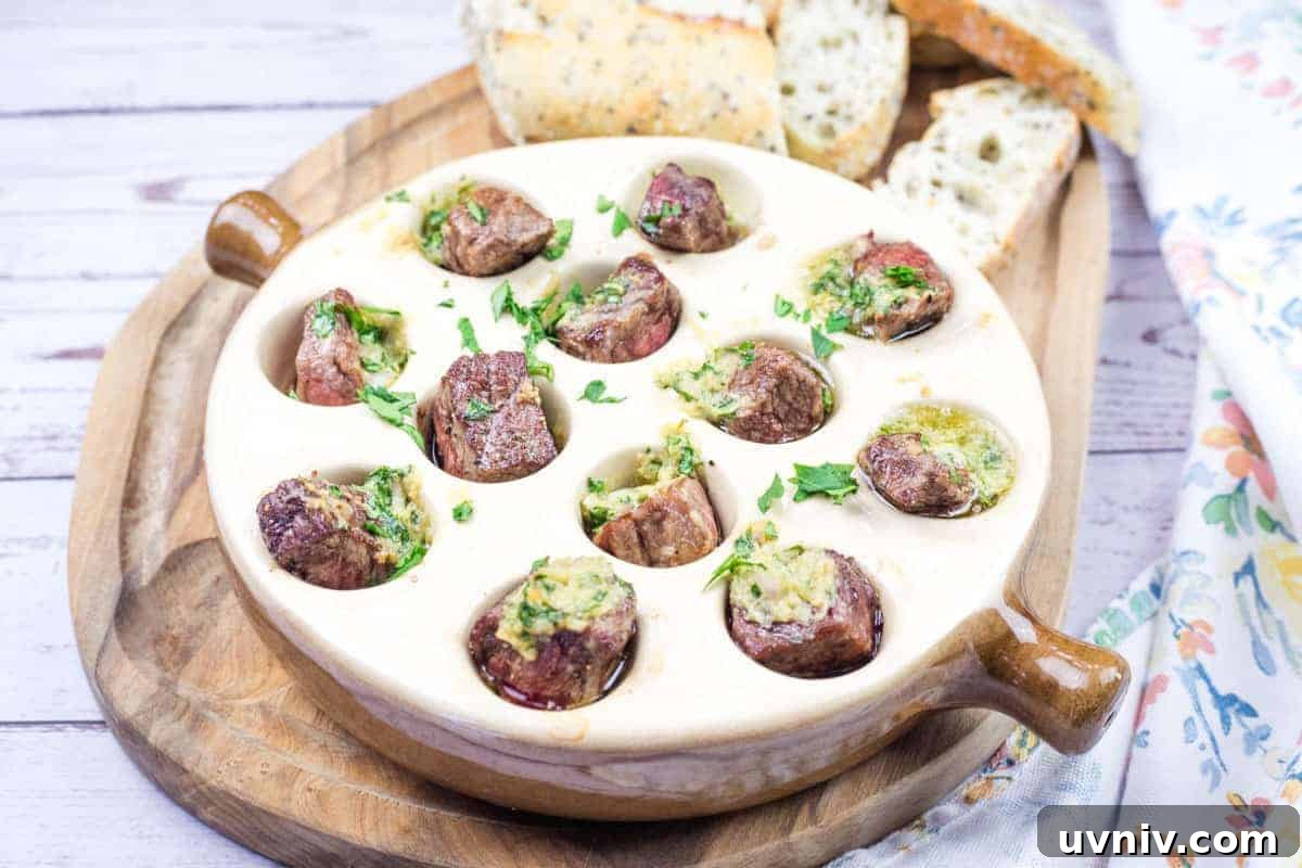 Garlic Butter Steak Bites Escargot-Style dish in a round ceramic plate with cooked snails topped with herbs and butter sauce, and slices of bread on a wooden board.