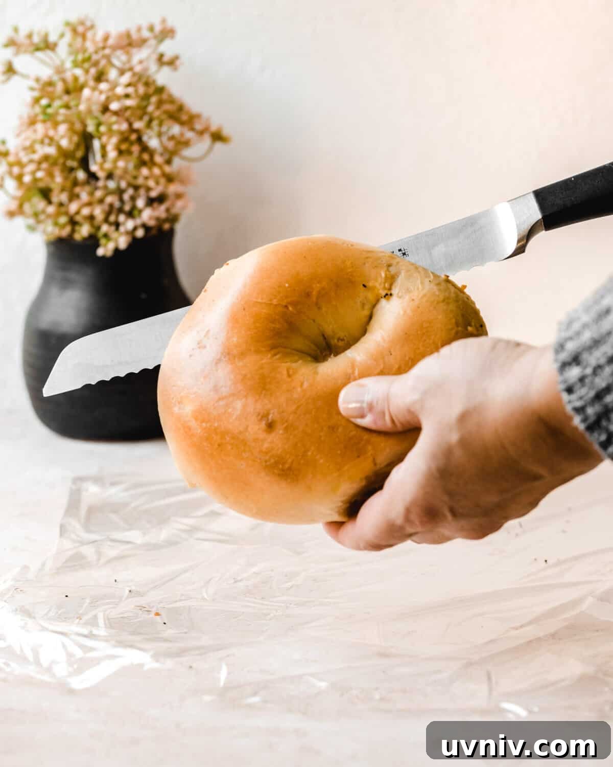 How Long Do Bagels Stay Fresh in the Fridge? 5 Hand holding a bagel while slicing it open with a serrated knife.