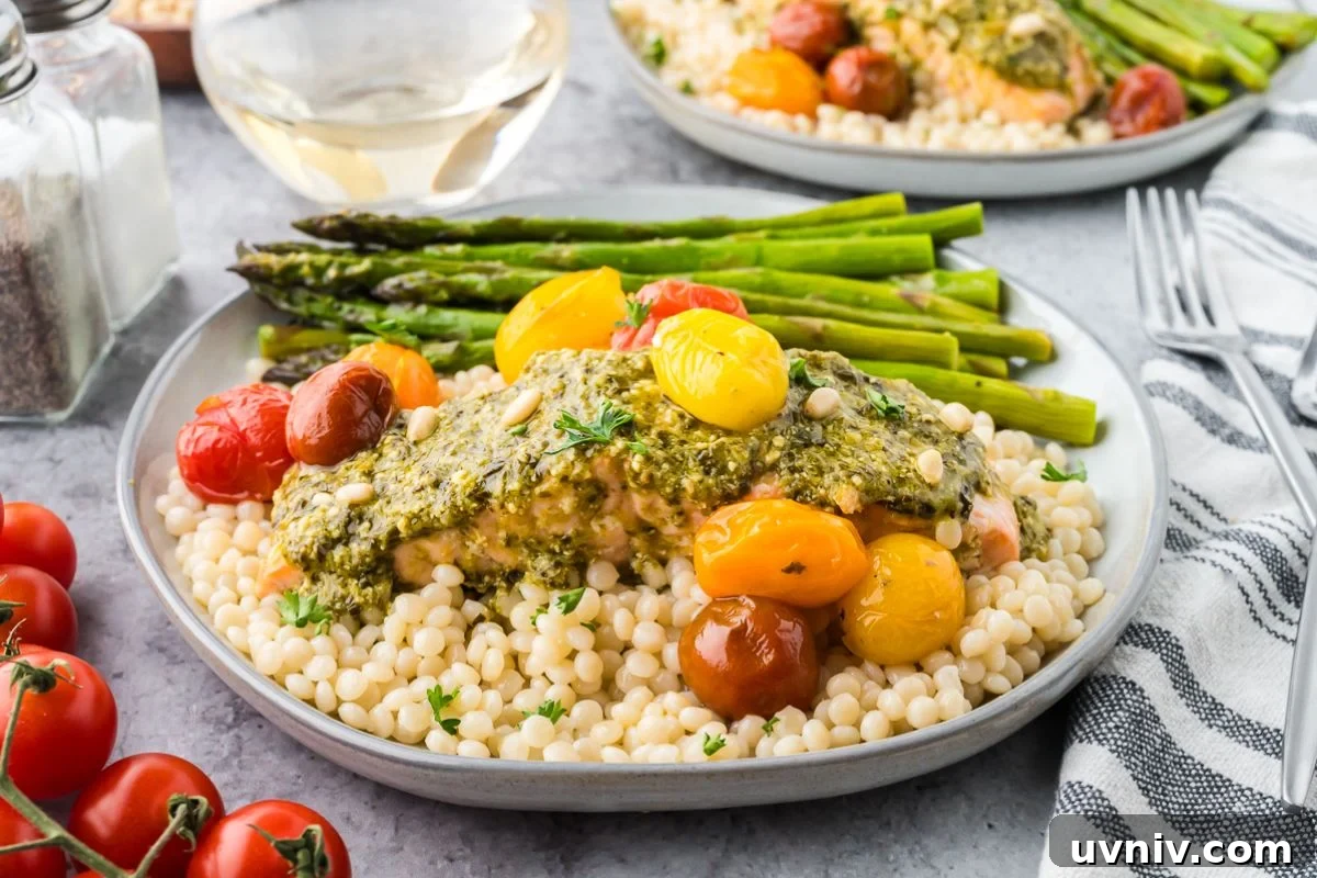 One-Pan Salmon and Roasted Asparagus Recipe 2 A plate of couscous topped with sheet pan salmon and asparagus, roasted tomatoes, and pesto, served with a glass of white wine.