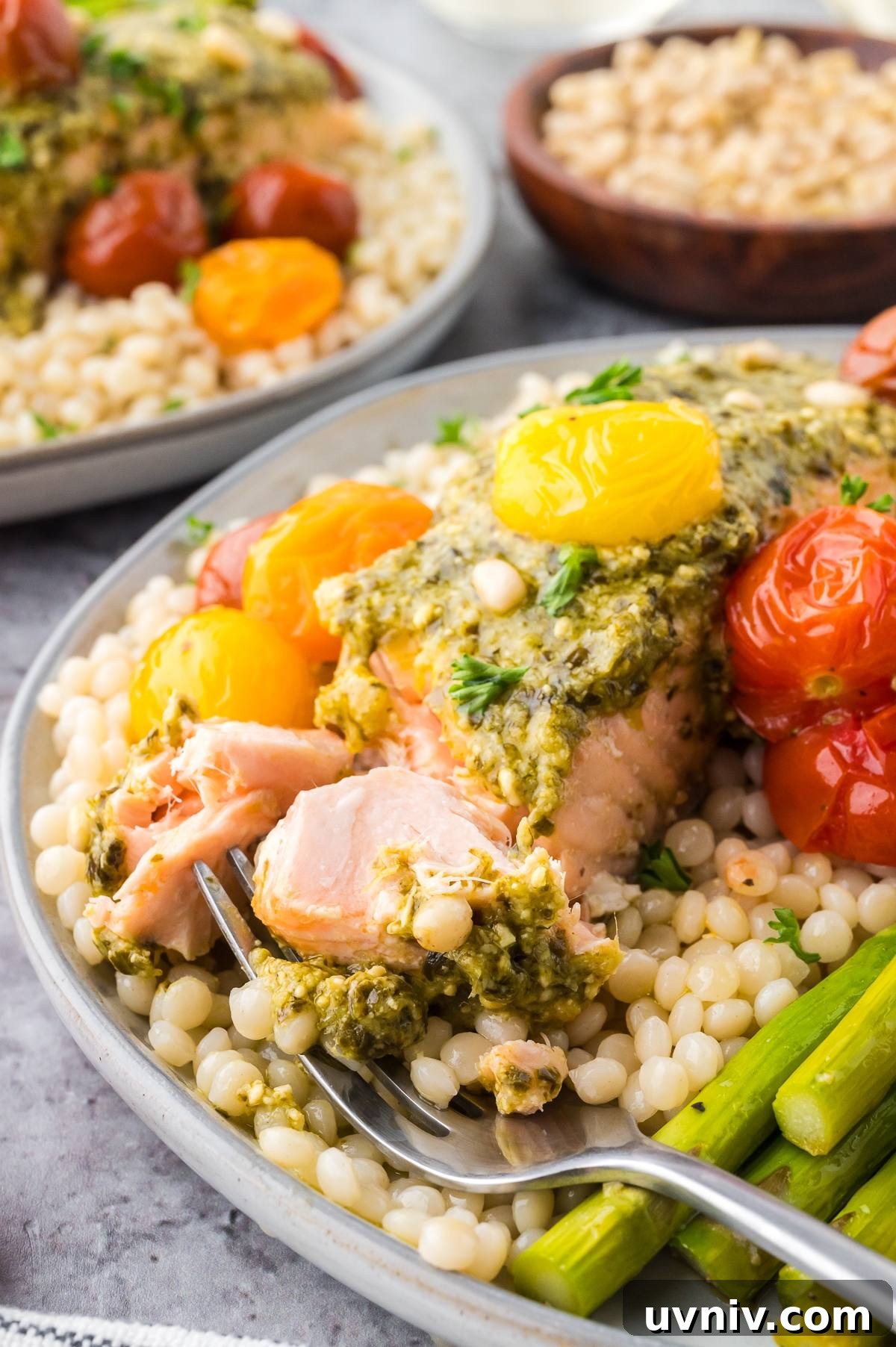 One-Pan Salmon and Roasted Asparagus Recipe 11 A plate of couscous with salmon, pesto sauce, cherry tomatoes, and asparagus, with a forkful of salmon.