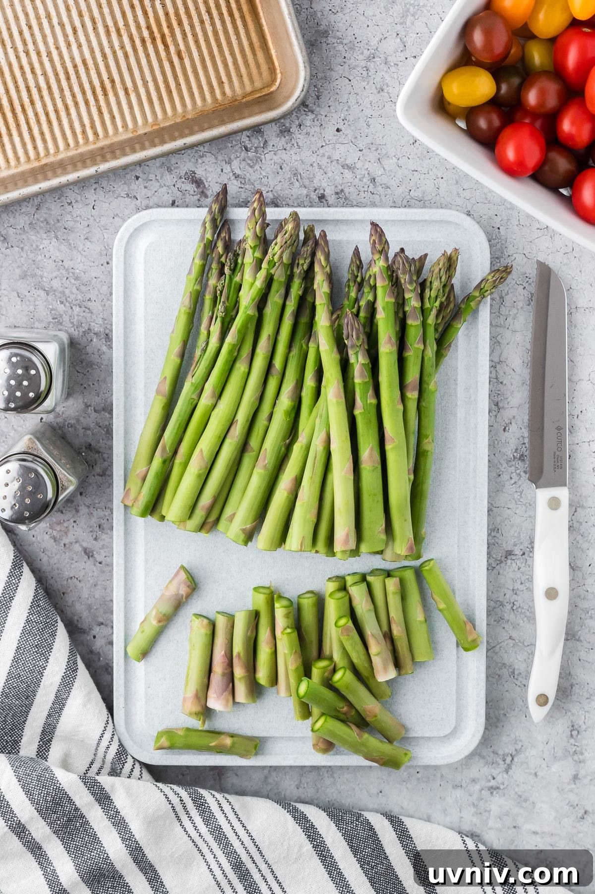 One-Pan Salmon and Roasted Asparagus Recipe 16 Fresh asparagus spears and chopped ends on a cutting board, with a knife, salt, pepper, and cherry tomatoes nearby.