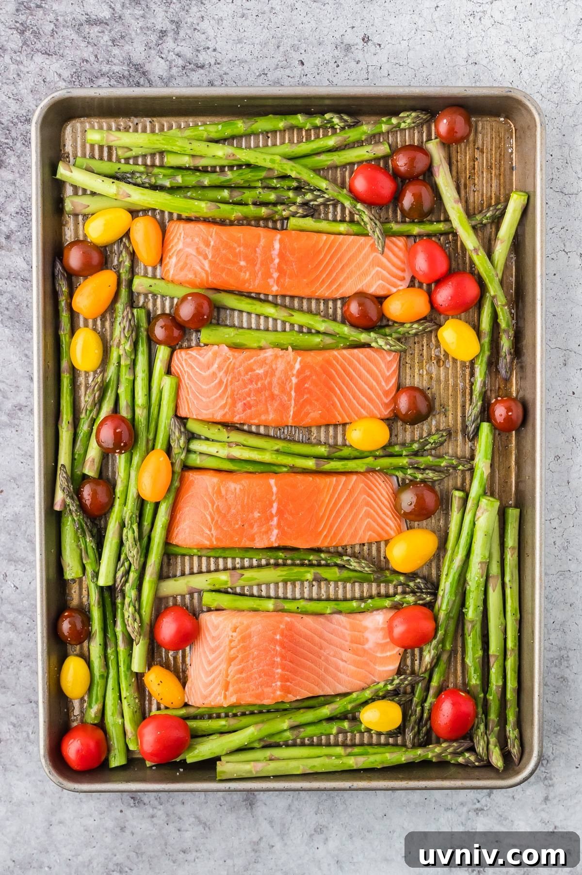 One-Pan Salmon and Roasted Asparagus Recipe 18 Four raw salmon fillets, asparagus stalks, and colorful cherry tomatoes on a baking sheet.