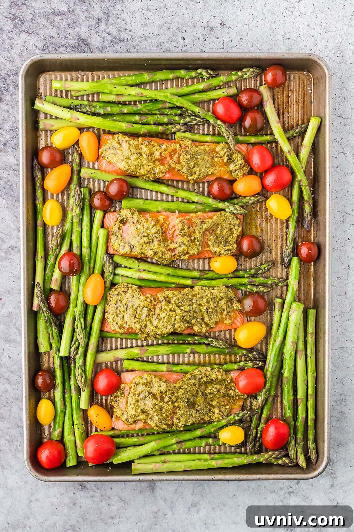 One-Pan Salmon and Roasted Asparagus Recipe 19 Sheet Pan Salmon and Asparagus with pesto, alongside vibrant red and yellow cherry tomatoes, ready for baking.