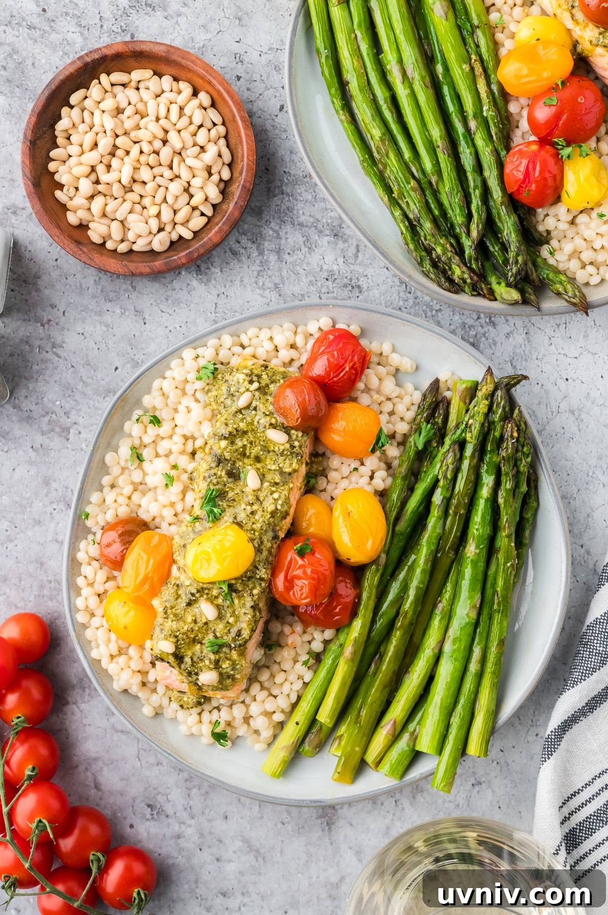One-Pan Salmon and Roasted Asparagus Recipe 5 Plate with couscous, pesto salmon, roasted tomatoes, and asparagus; bowl of pine nuts and tomatoes nearby.