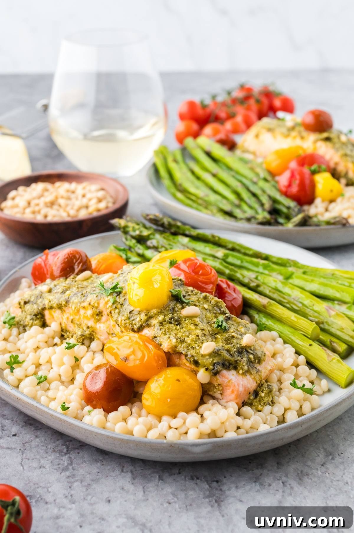 One-Pan Salmon and Roasted Asparagus Recipe 6 A plate with salmon, couscous, asparagus, and cherry tomatoes, with a glass of white wine in the background.