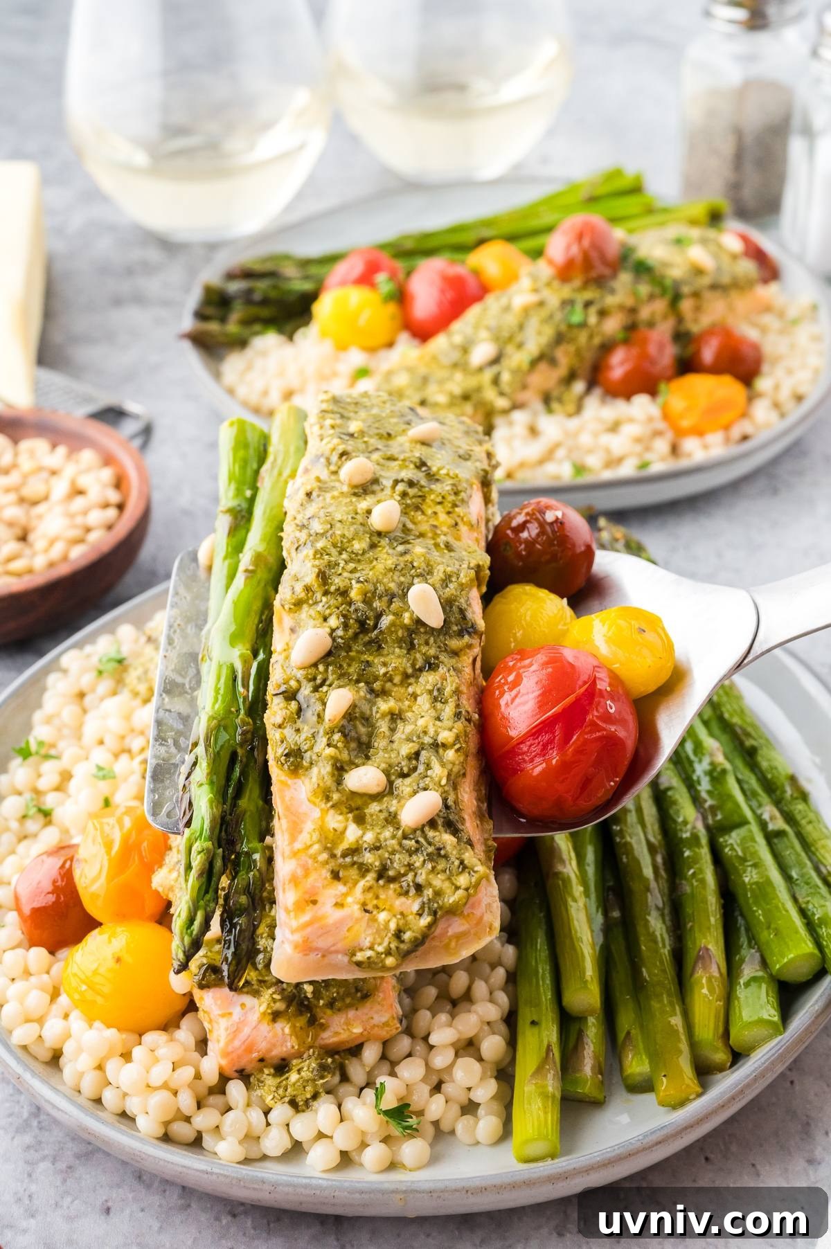 One-Pan Salmon and Roasted Asparagus Recipe 9 A plate with pesto salmon, asparagus, cherry tomatoes, and couscous, served with pine nuts on top.