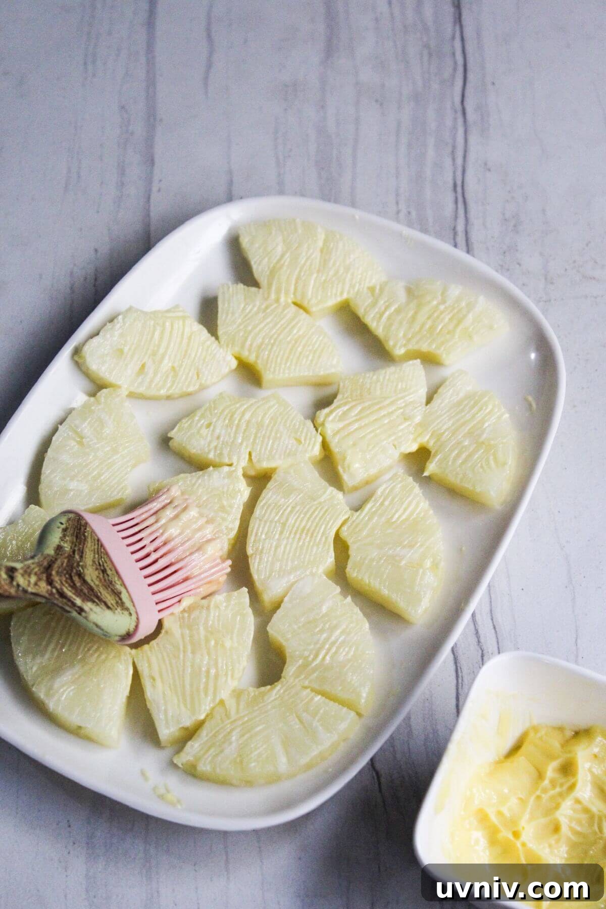 Crispy Caramelized Pineapple in the Air Fryer 6 A white plate with sliced pineapple getting butter brushed on.