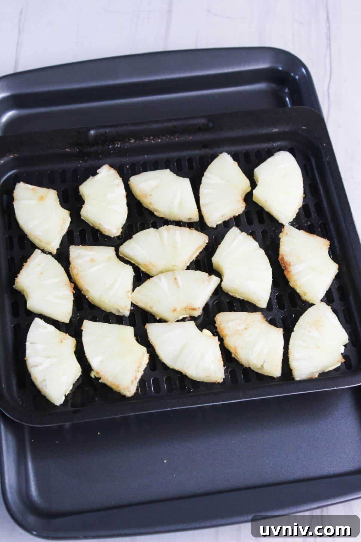 Crispy Caramelized Pineapple in the Air Fryer 8 Sliced pineapple on a an air fryer tray.