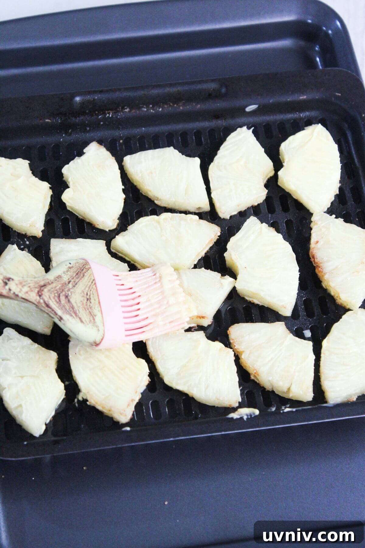 Crispy Caramelized Pineapple in the Air Fryer 9 Sliced pineapple on an air fryer tray being brushed with butter.