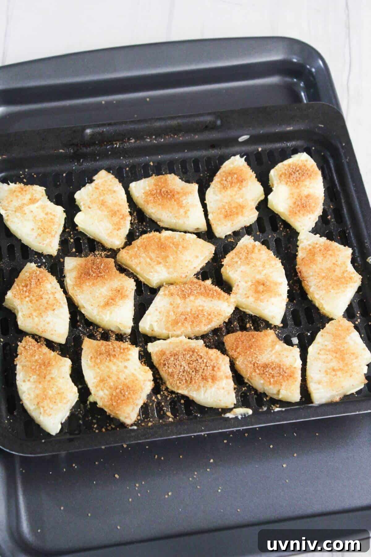 Crispy Caramelized Pineapple in the Air Fryer 10 An air fryer tray with pieces of pineapple coated in brown sugar on it.