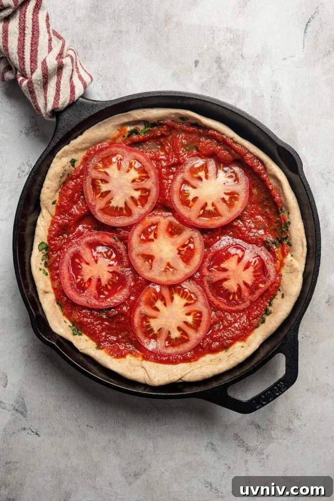 This deep dish pizza recipe with homemade herbed crust, tomatoes, and lots of melty cheese will bring Pizza Night to your kitchen each week. Adding the tomato sauce and sliced tomatoes to the dough.