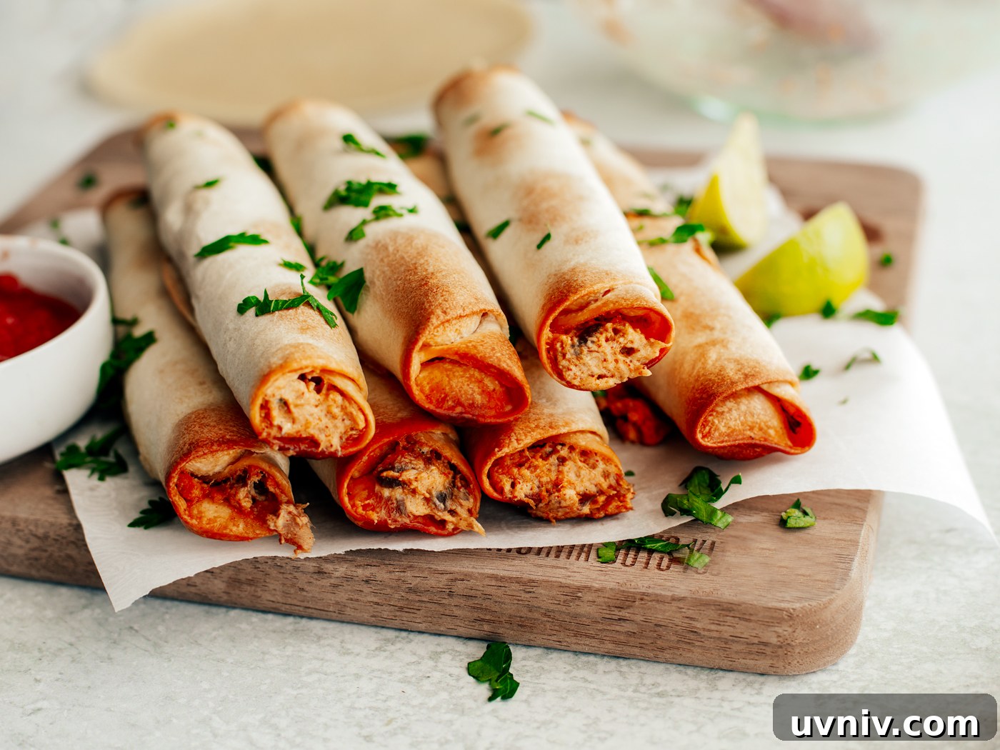 Baked flautas in a wooden serving board with a dipping bowl of salsa.