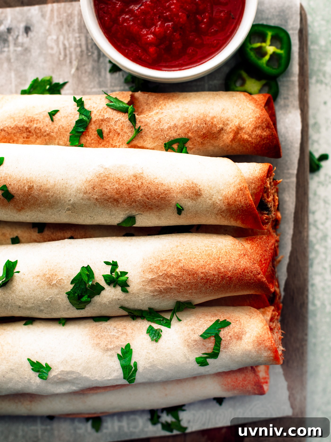 Close up of baked flautas on parchment-covered serving board.