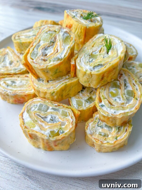 Crispy Zucchini Egg Roll Recipe with Garlic Dipping Sauce 3 A plate of Zucchini Egg Roll pinwheels filled with cream cheese and diced vegetables, garnished with a sprig of fresh dill, displayed on a white plate.