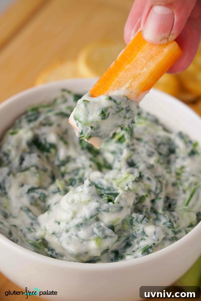 Labor Day Cooking & Baking Deals: Top Discounts on Kitchen Gear 8 Spinach dip in a white bowl with a carrot being dipped into it.