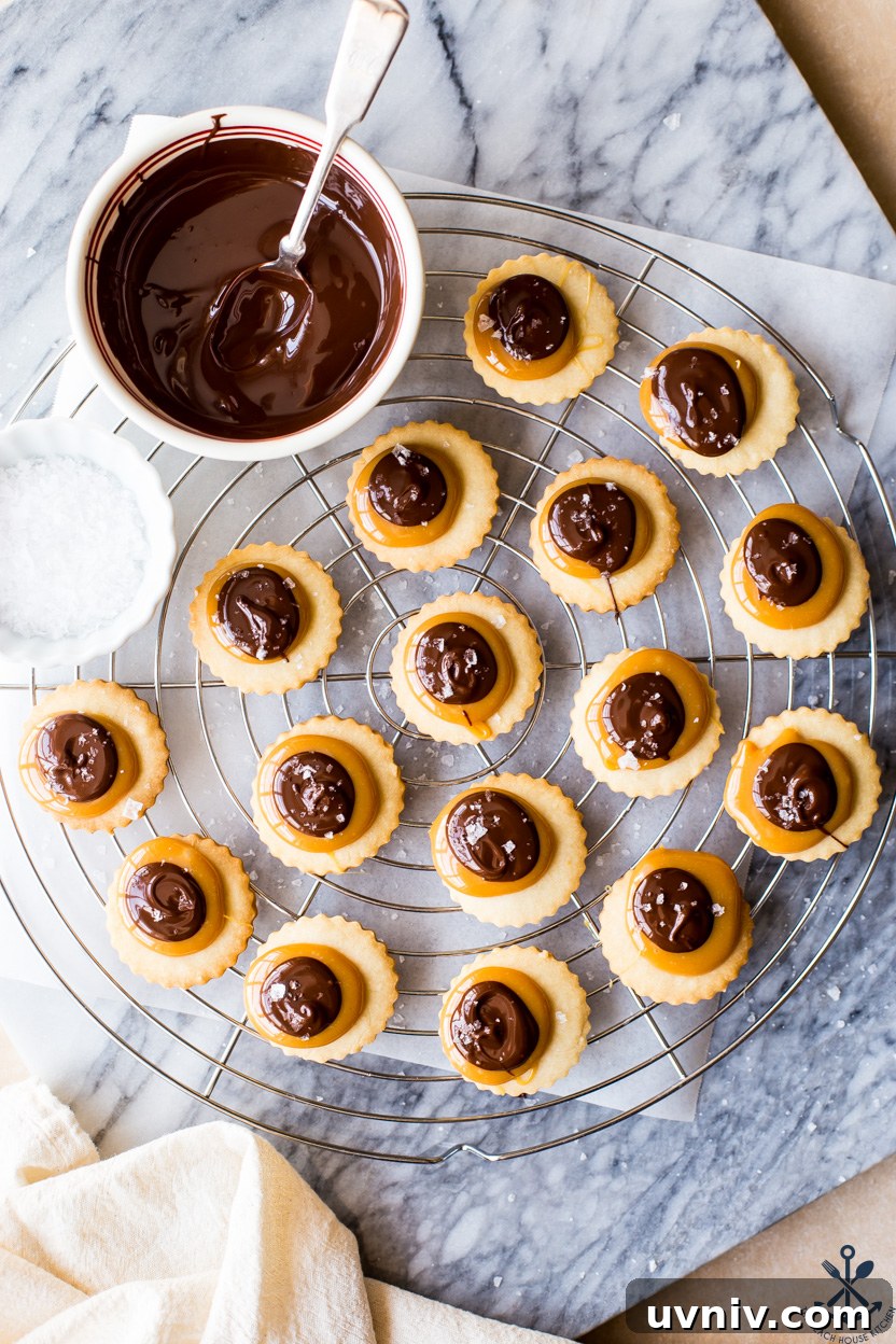 Twix Cookie Bars: Chewy Caramel Chocolate Treat Recipe 8 Overhead photo of Twix cookies on a round wire rack with a bowl of melted chocolate and a small bowl of sea salt
