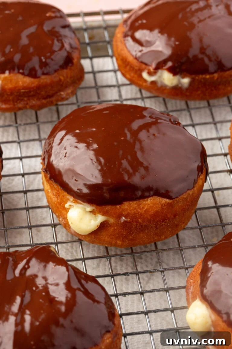 Boston cream donuts with chocolate glaze and creamy filling are cooling on a wire rack.