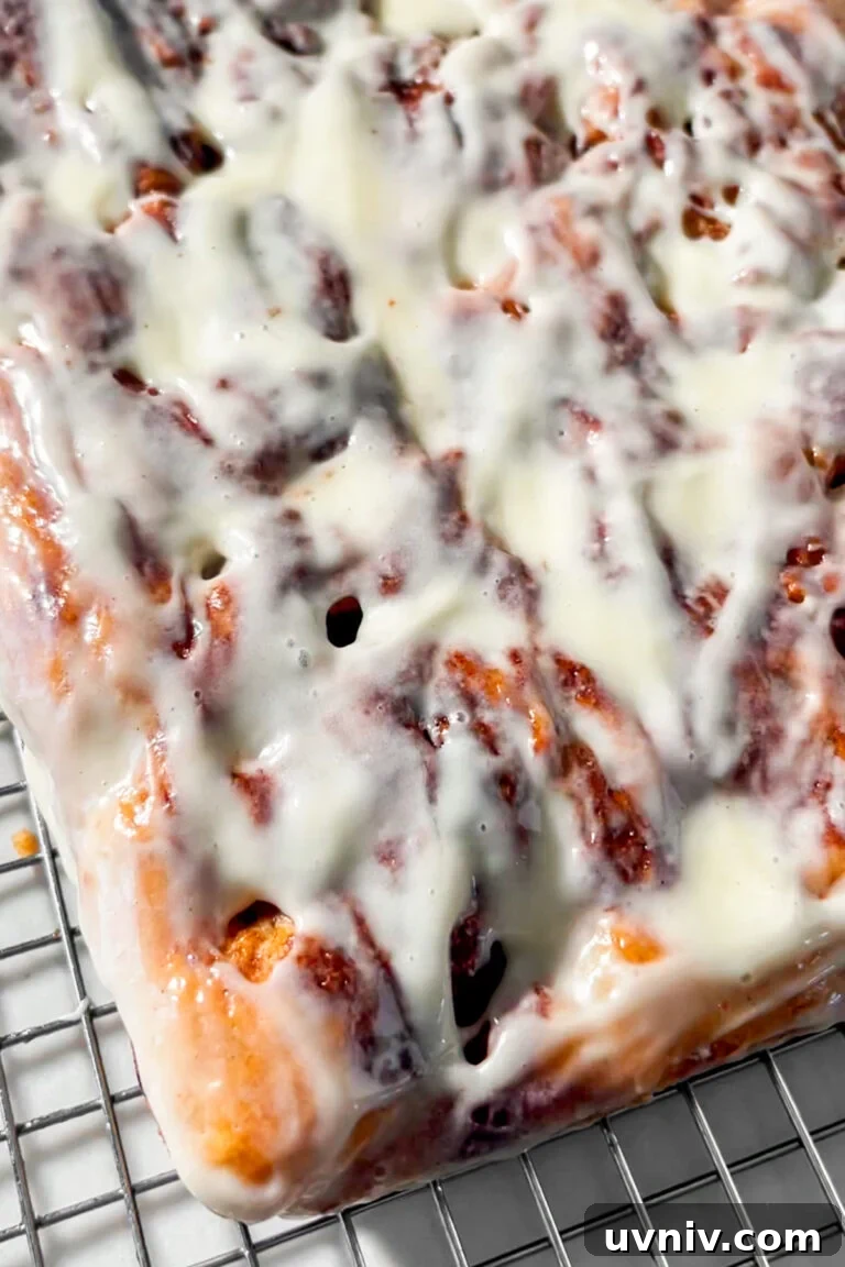 A close-up of a rectangular gluten-free cinnamon roll focaccia slab covered in creamy white icing.