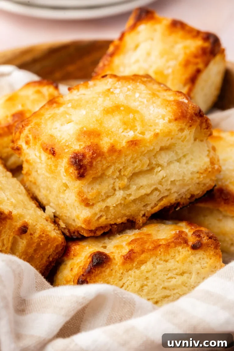A close-up of golden, flaky homemade biscuits stacked in a basket.