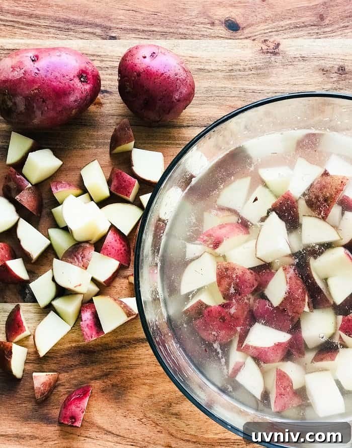 Creamy Loaded Potato Salad Made in the Instant Pot 5 diced red potatoes on a wooden board and in a clear bowl with water.