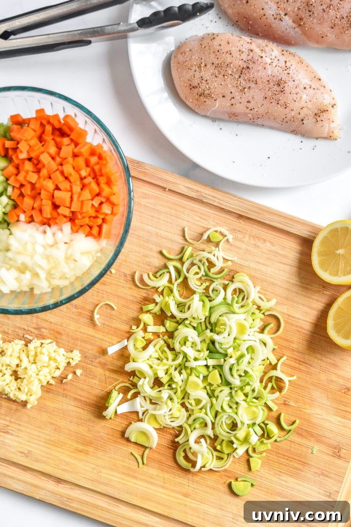sliced leeks on a cutting board with other vegetables and seasoned chicken breast on a plate. 