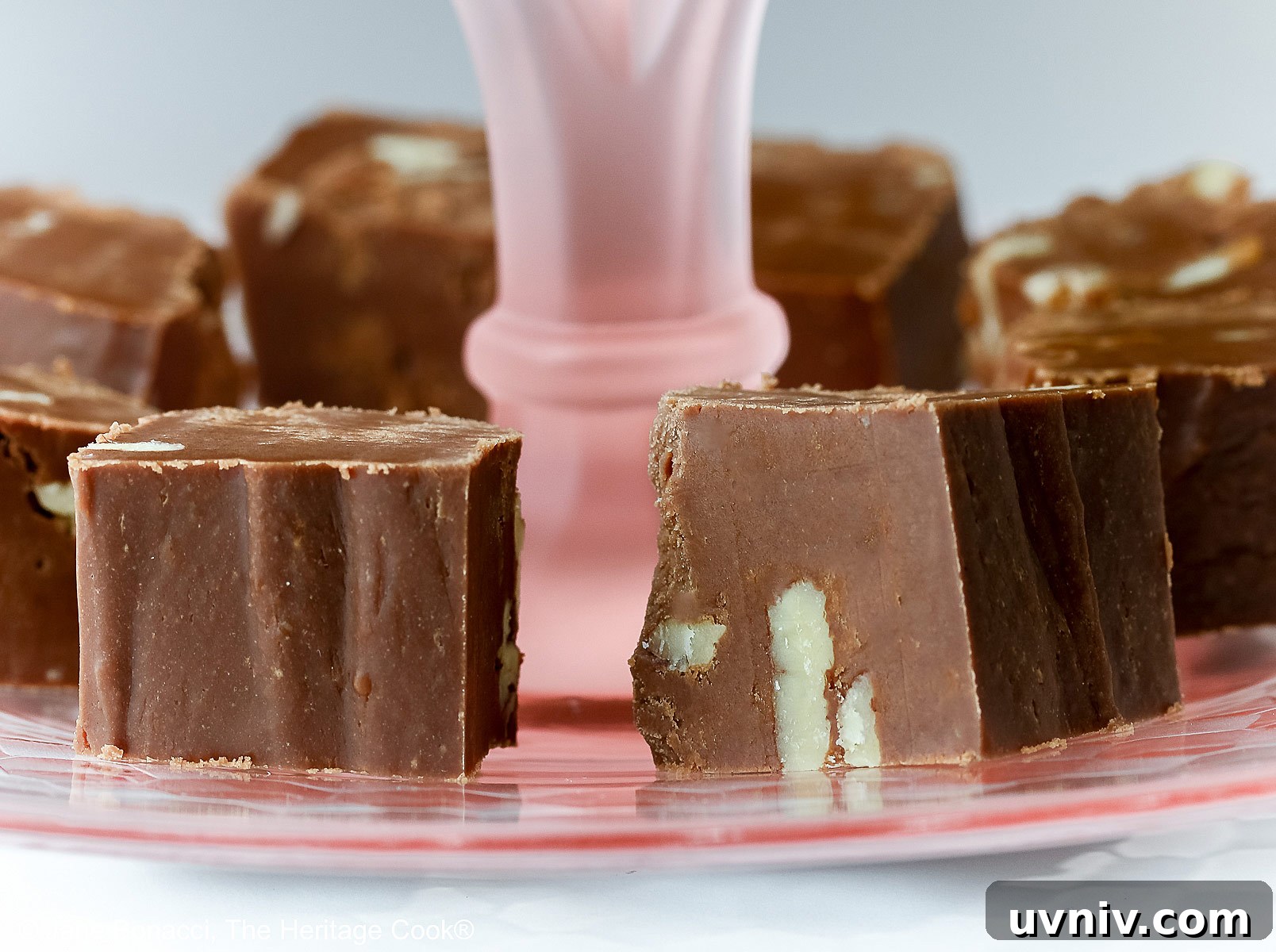 Squares of easiest fudge with nuts circling and stacked on a scalloped pink glass serving plate © 2024 Jane Bonacci, The Heritage Cook.