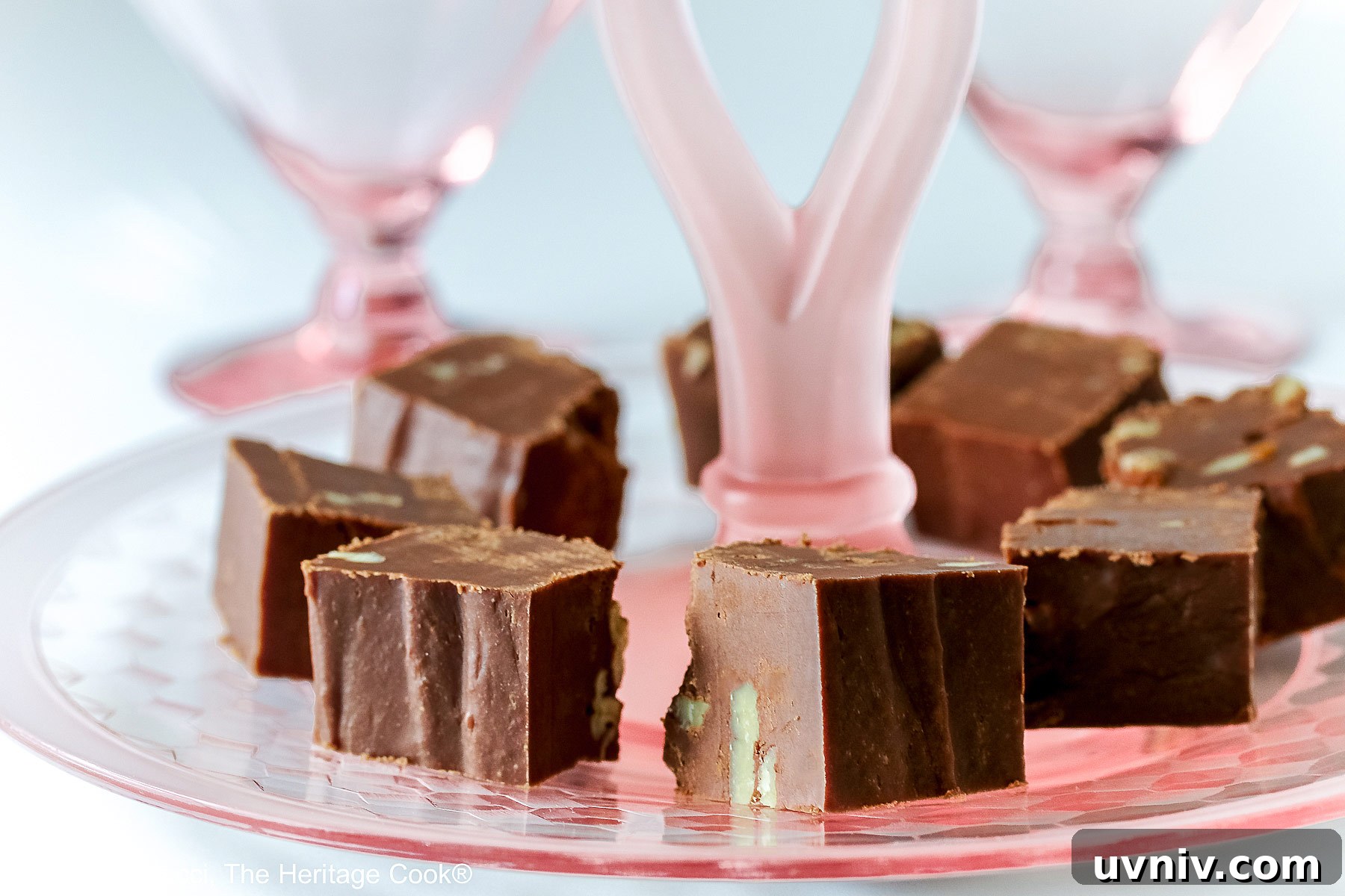 World’s Simplest Gluten-Free Fudge Recipe 4 Squares of easiest fudge with nuts circling and stacked on a scalloped pink glass serving plate © 2024 Jane Bonacci, The Heritage Cook.
