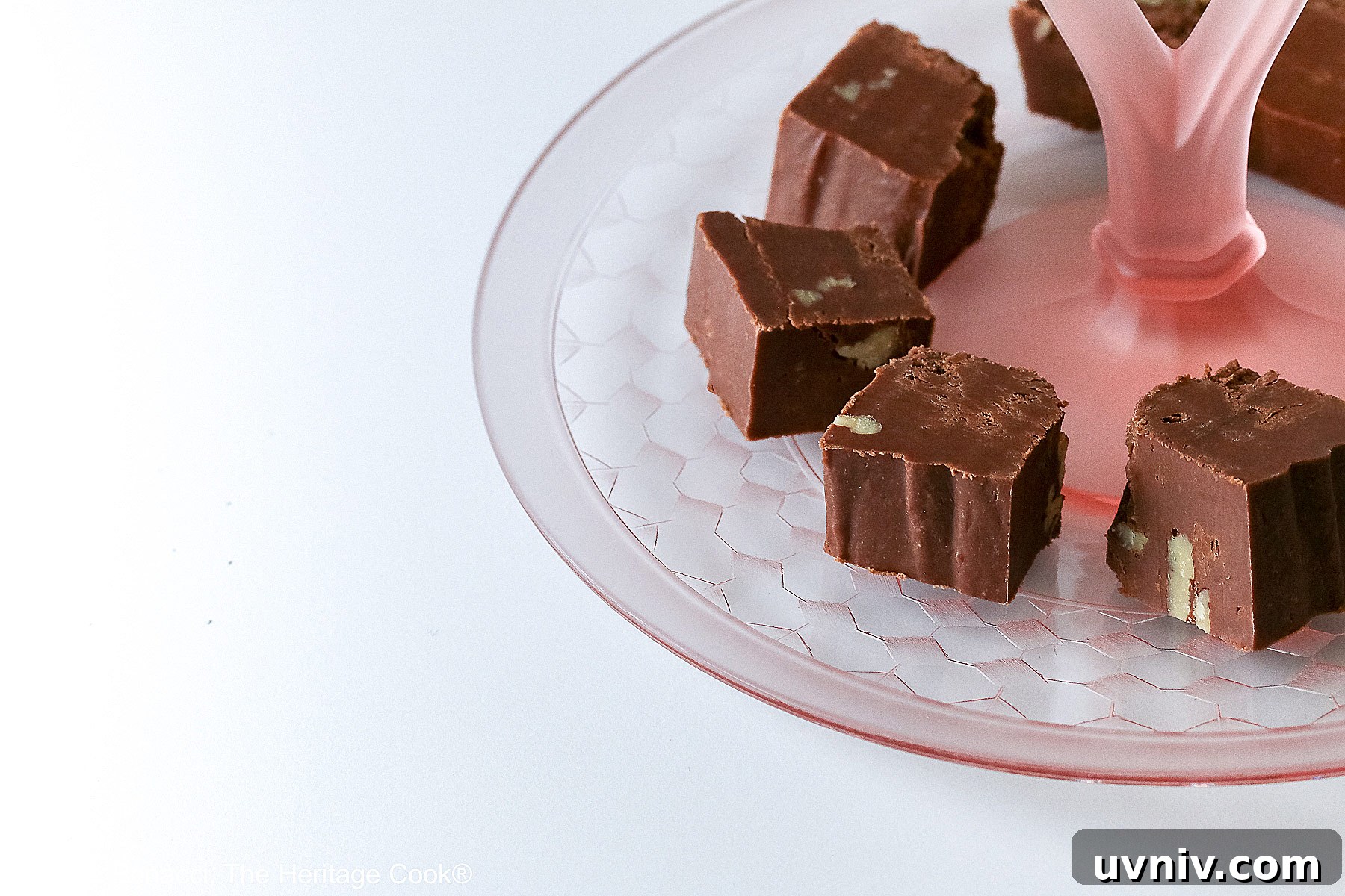 World’s Simplest Gluten-Free Fudge Recipe 5 Squares of easiest fudge with nuts circling and stacked on a scalloped pink glass serving plate © 2024 Jane Bonacci, The Heritage Cook.