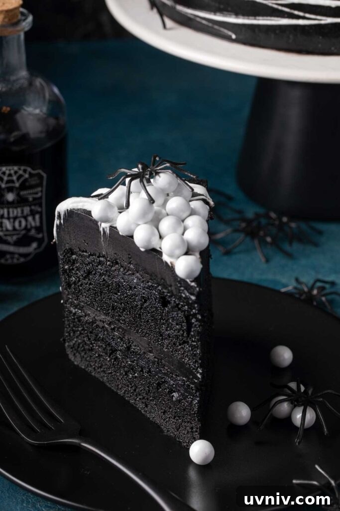 Slice of layered black velvet cake with black cocoa buttercream topped with candy sixlets.
