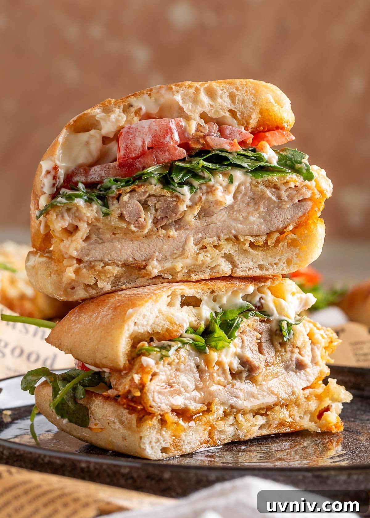 Stacked halves of a crispy chicken sandwich showing the juicy interior of the air-fried chicken thigh, fresh arugula, tomato, and creamy mayo on toasted sandwich rolls.