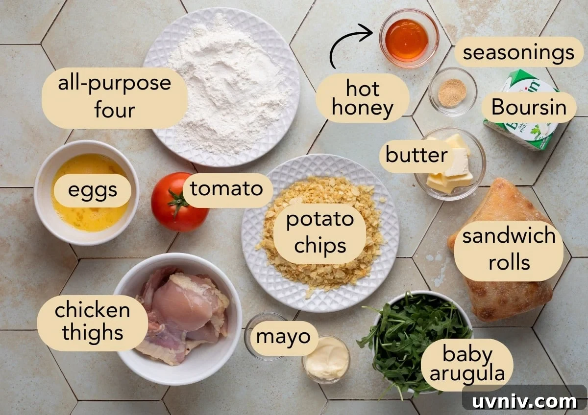 Flat lay of labeled ingredients for a crispy chicken sandwich with hot honey, including chicken thighs, crushed potato chips, sandwich rolls, Boursin cheese, baby arugula, tomato, mayo, eggs, flour, butter, hot honey, and seasonings on a tiled surface.