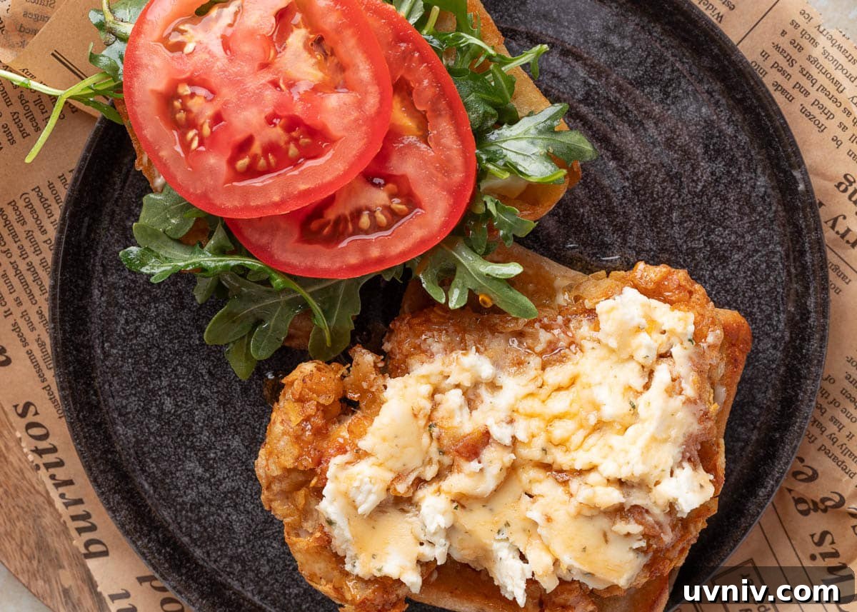 Overhead view of an open-faced air fryer chicken sandwich with potato chip-crusted chicken topped with Boursin and hot honey on one side, and fresh arugula and tomato slices on the other, served on a toasted ciabatta roll.