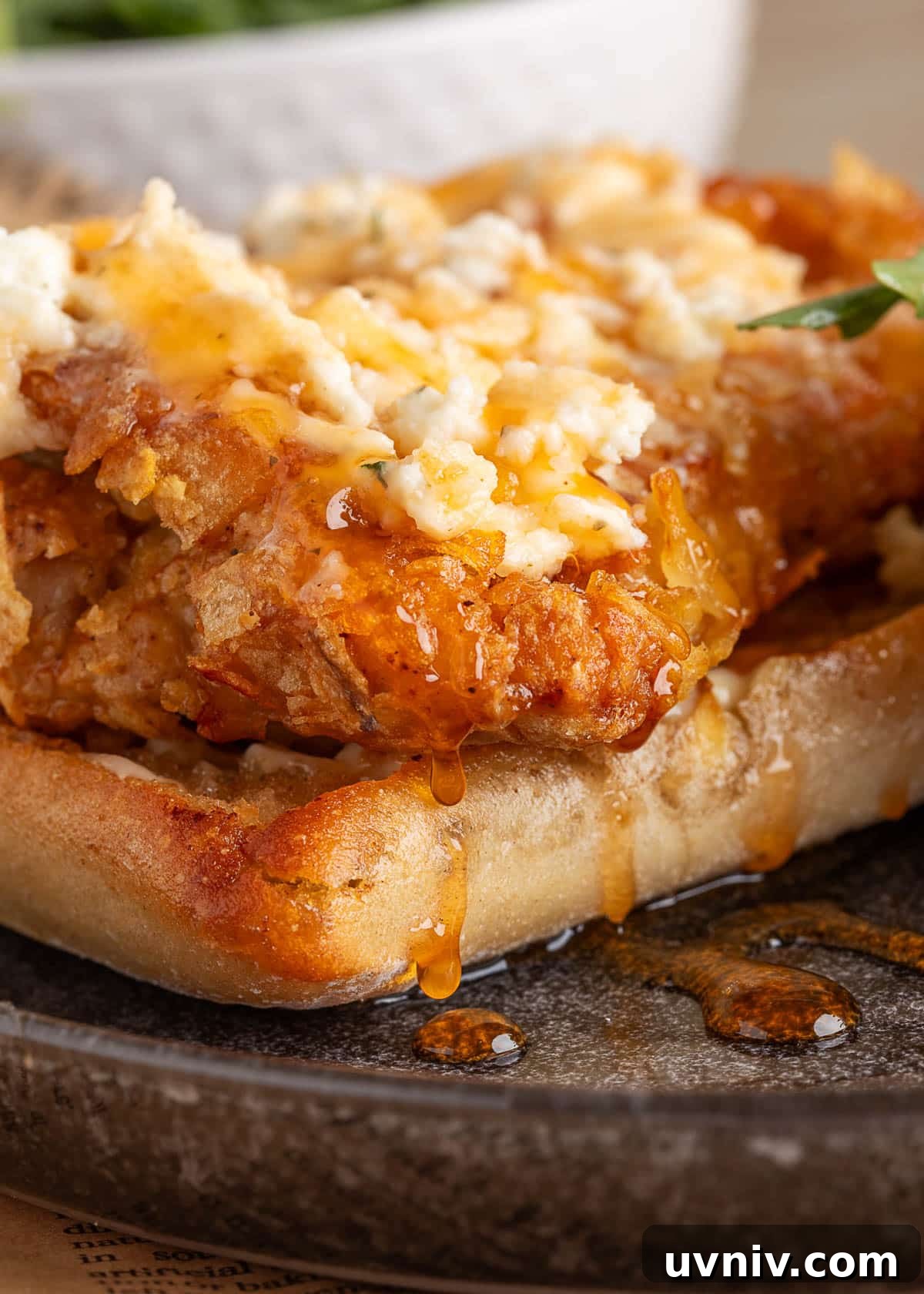 Macro shot of the sandwich’s crispy chicken topped with Boursin cheese and a thick drizzle of golden honey pooling onto the plate, showcasing rich textures and shine.