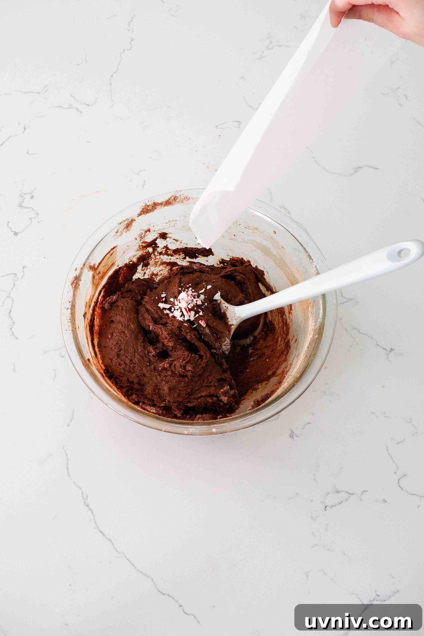 Decadent Peppermint Brownies Recipe for Holiday Baking 11 A hand funnels crushed candy cane pieces into a glass bowl of brownie batter.