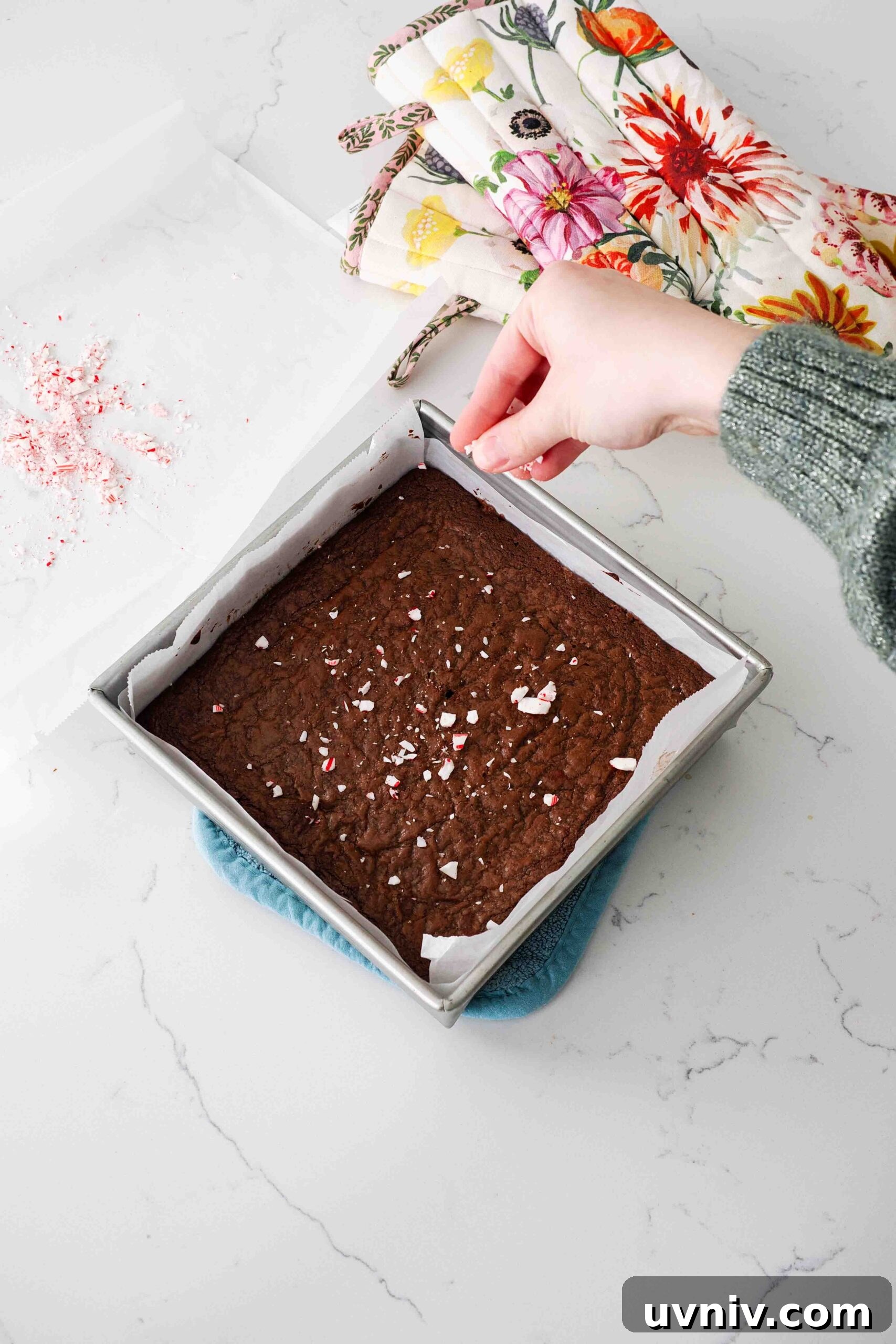 Decadent Peppermint Brownies Recipe for Holiday Baking 13 A hand sprinkles crushed candy canes over a hot pan of brownies.