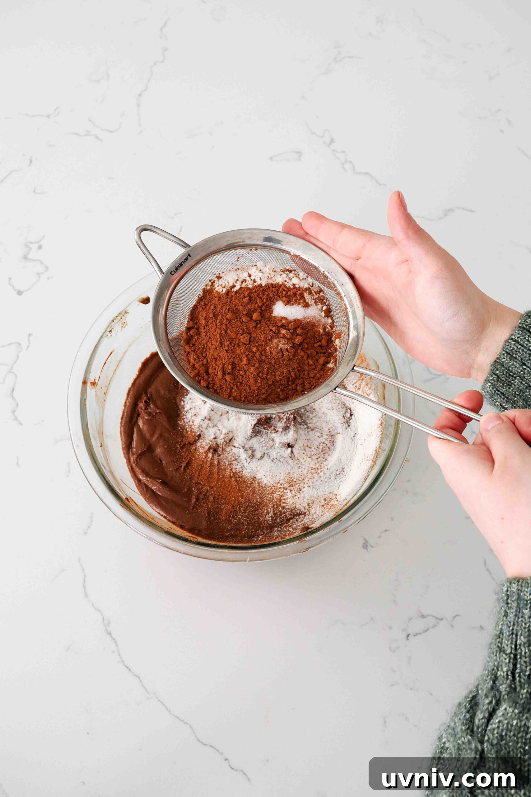 Decadent Peppermint Brownies Recipe for Holiday Baking 10 Two hands sift flour and cocoa powder into a glass bowl with brownie batter.