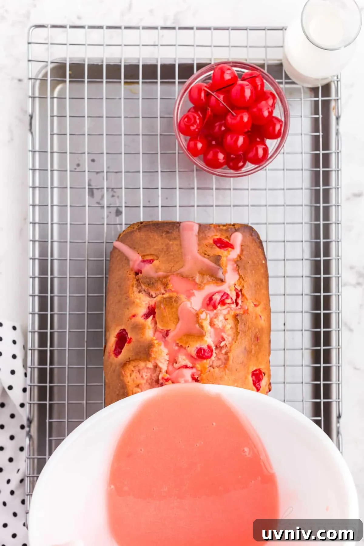 glaze poured on top of cherry bread on wire cooling rack over cookie sheet next to cherries