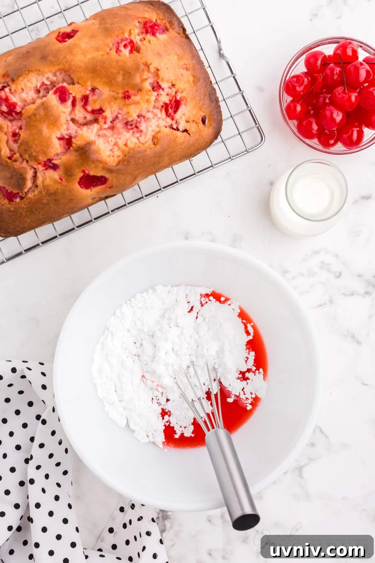 Powdered sugar mixed with cherry juice in small dish for glaze with a whisk next to baked cherry bread.