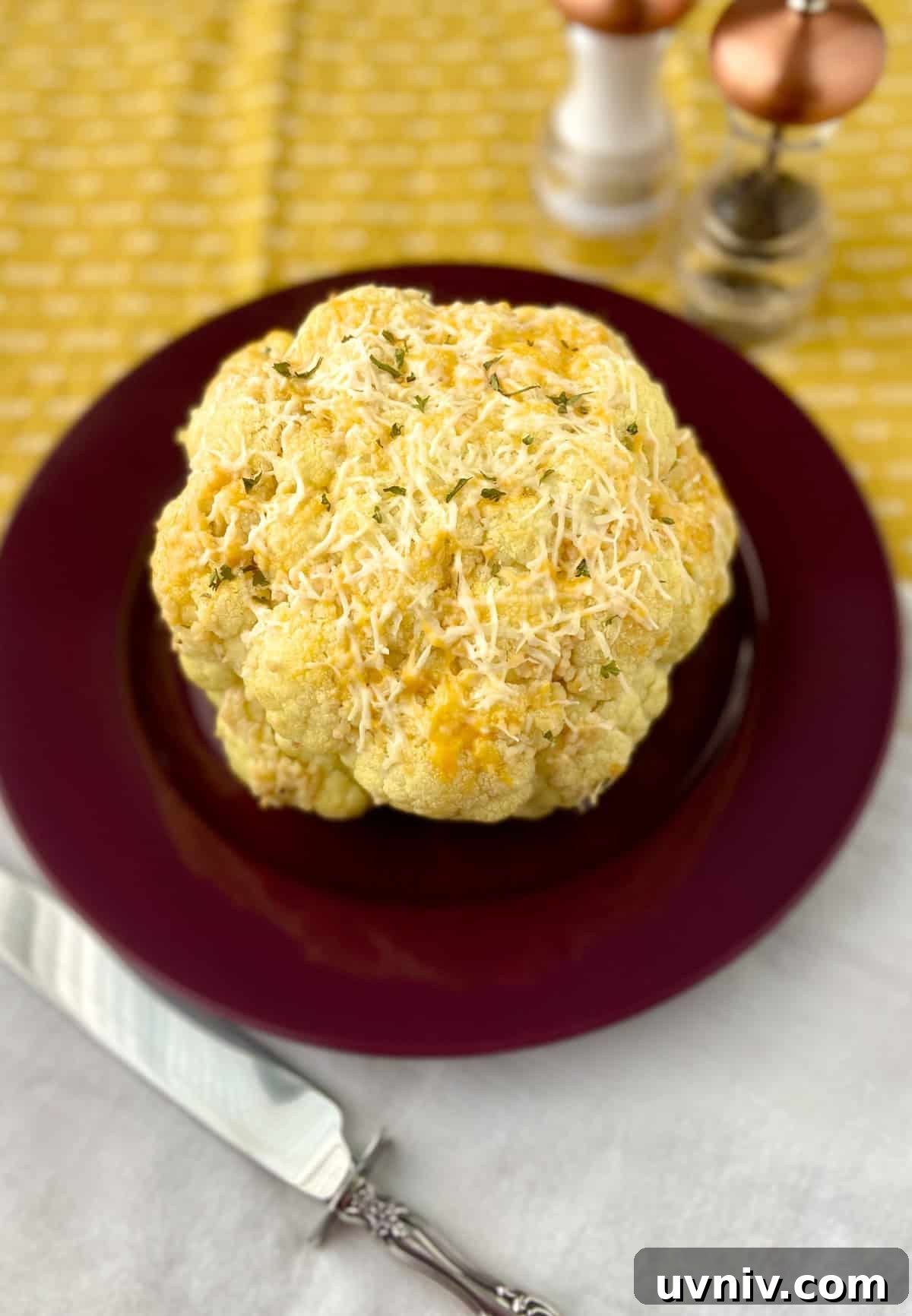 Whole roasted cauliflower with cheese on red plate.