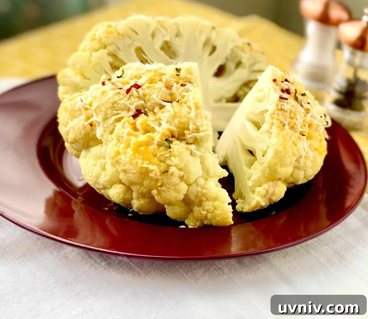 Whole roasted cauliflower with cheese cut into quarters on red plate.