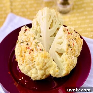 Whole roasted cauliflower on red plate.
