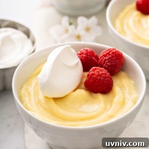 Vanilla pudding in a small white bowl, topped with whipped cream and fresh raspberries