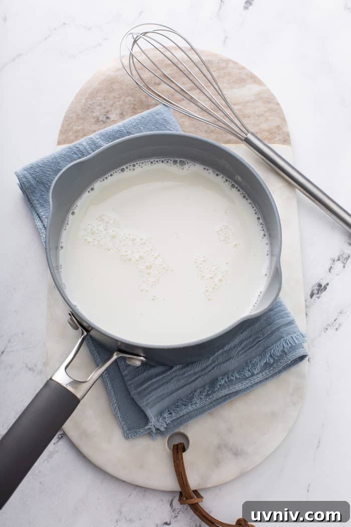Milk and sugar in a saucepan set on a blue towel on a marble countertop