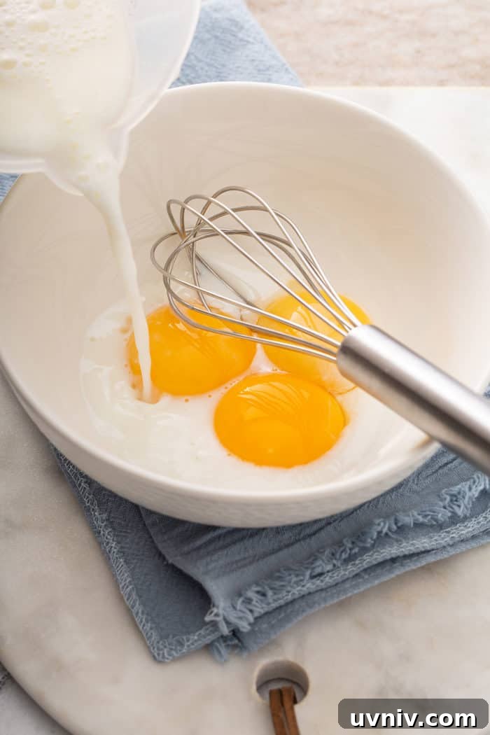 Hot milk being streamed into a white bowl with 3 egg yolks