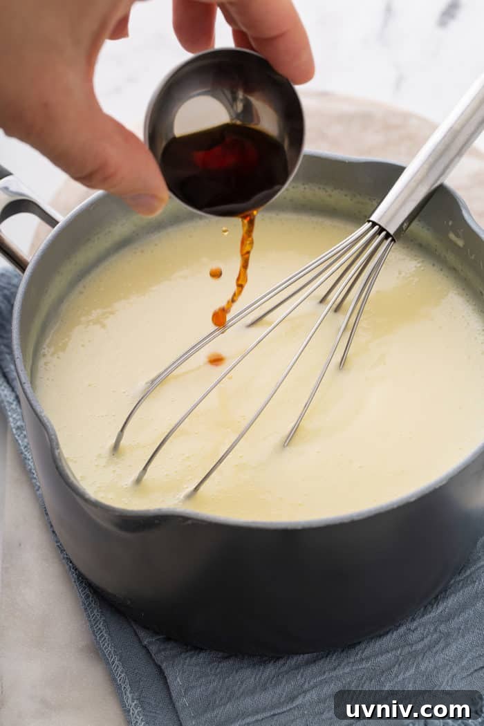 Hand pouring vanilla extract into vanilla pudding in a saucepan