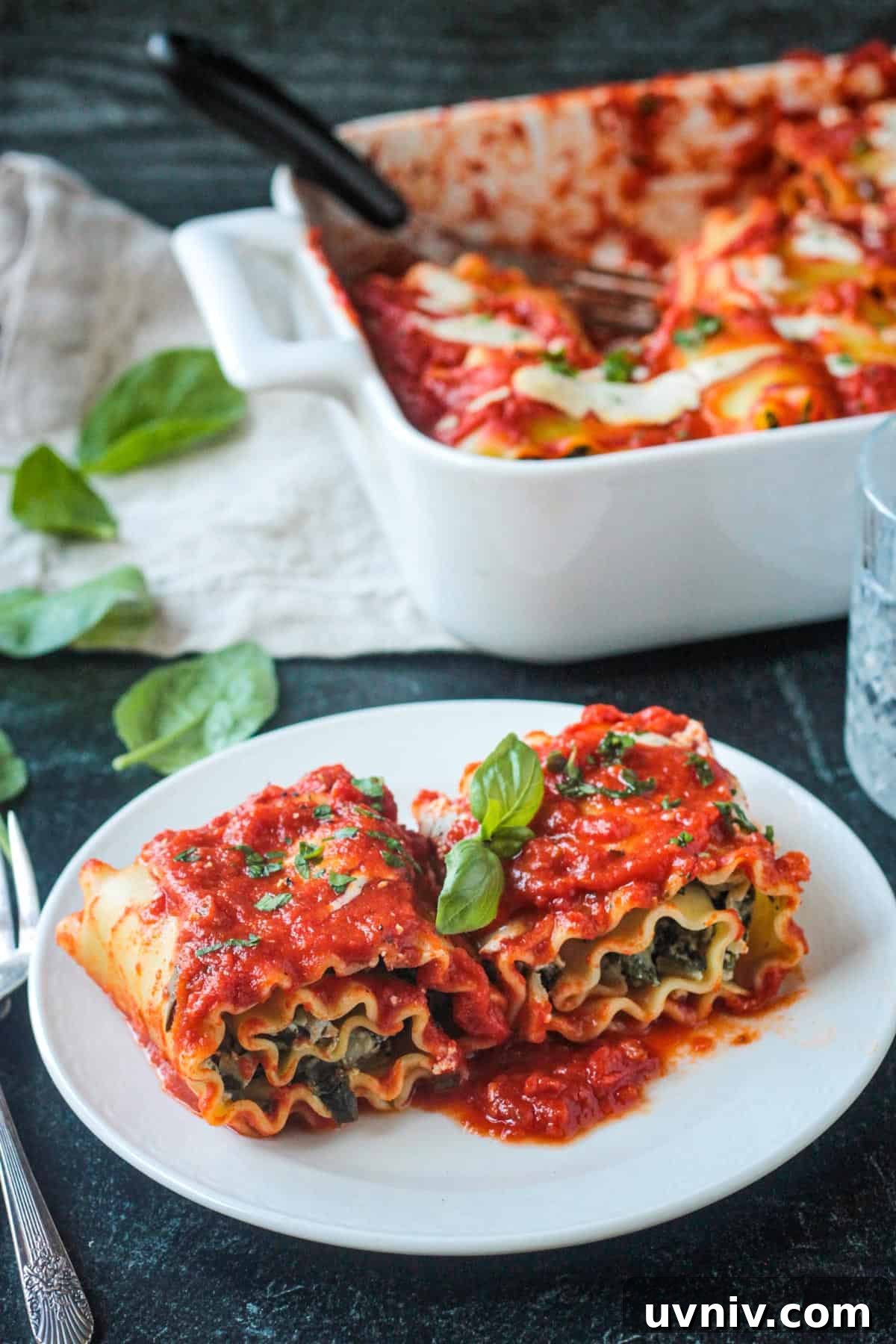 Two lasagna roll ups on a white plate garnished with fresh basil.